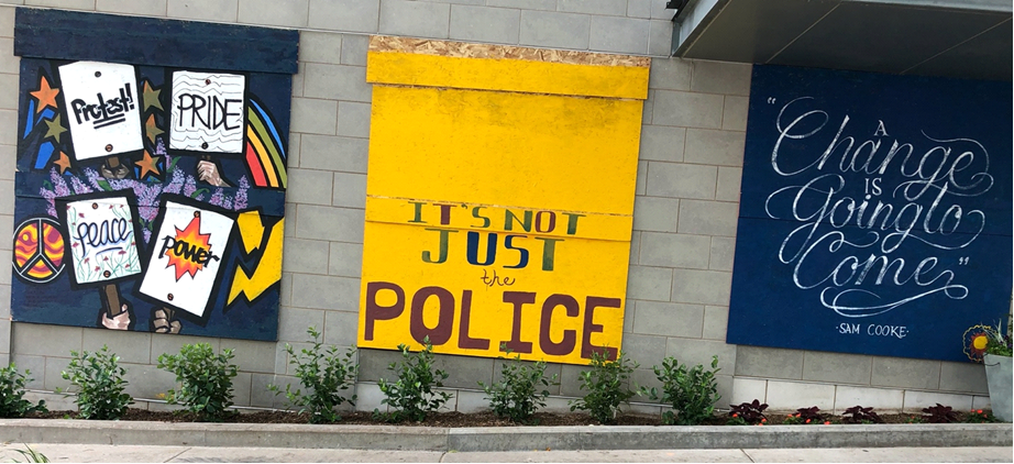 Windows boarded up with plywood, covered with colorful painted racial justice slogans